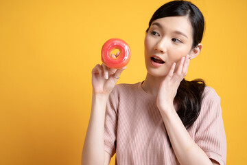 Young and cute Asian girl holding delicious donut image isolated on yellow background