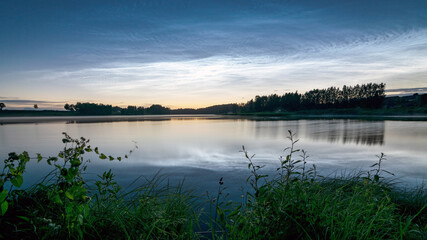 night landscape with white silver clouds over the lake, blurred foreground, charming cloud reflections in the lake water, summer night