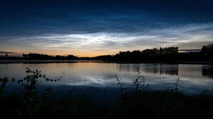 night landscape with white silver clouds over the lake, blurred foreground, charming cloud reflections in the lake water, summer night