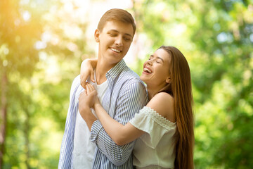 Fototapeta premium Lovely young girl laughing and hugging her handsome boyfriend at summer park