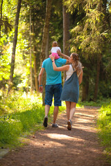 Mother, father and baby walking in the park. Summer time. Happy family spent time together outdoors. The child sits on his fathers shoulders.