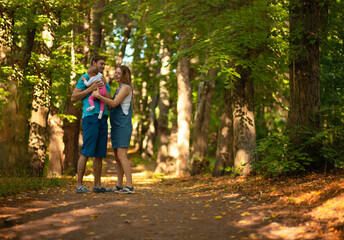 Fototapeta na wymiar Mother, father and baby walking in the park. Summer time. Happy family spent time together outdoors. Man holds his daughter in the arms.