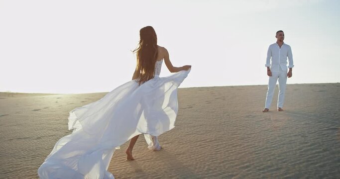 Beautiful romantic couple in the white dress code in the middle of the amazing landscape with the white sand walking around