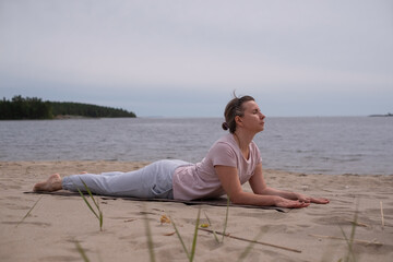 Fototapeta premium Woman doing Cobra Yoga Stretch on yoga mat in beach