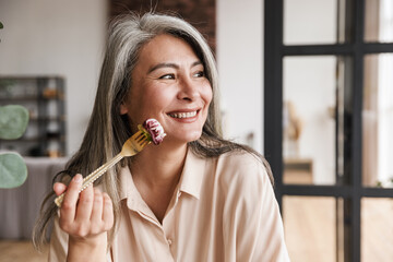 Woman sitting at kitchen indoors at home while eating salad.