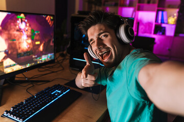 Image of cheerful man taking selfie photo while playing video game