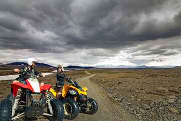 Happy smiling ATV quad driving man and woman traveling down a gravel road in Kaldidalur desert,...
