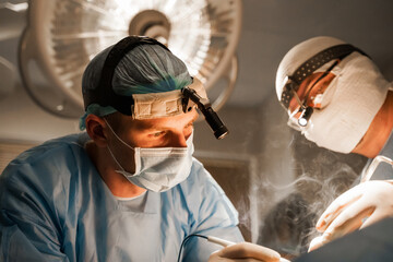 2 surgeons with headlamp do plastic operation in medical clinic. Chest augmentation plastic...