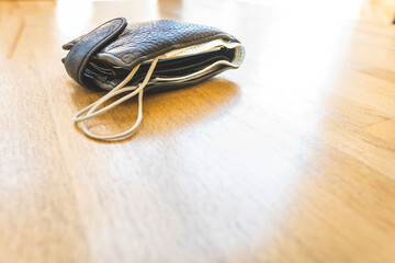 Black bulky wallet with facial mask in it laying on the light wooden textured surface with blank space. Concept of safety regulations in restaurants and public places during global pandemic.
