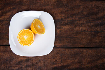 orange on a white plate on a rustic wooden surface with a black background. Top view.