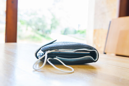 Balck bulky wallet with facial mask in it laying on the light wooden textured surface with blank space. Concept of safety regulations in restaurants and public places during global pandemic.