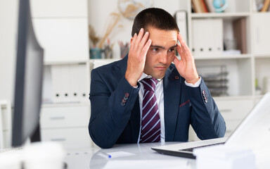 Portrait of troubled businessman looking worriedly at laptop screen in office..