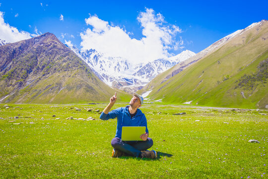 Male person in csualclothes  lays on the grass and points his finger up with mountains in the background. Inspiration and new ideas born in nature concept. Backgorud image of creativity