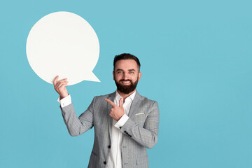 Happy young CEO pointing at blank speech bubble on blue background, space for design