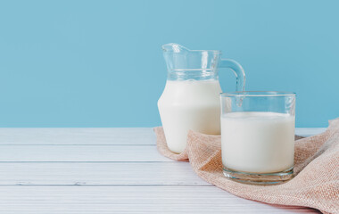 Natural fresh milk in a glass and pitcher, placed on a napkin on a wooden table on a blue background. Eating for good health