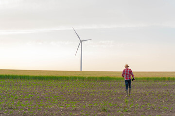 Young farmer walking in the field. Wind mill in background.