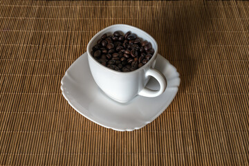 Roasted coffee grains in a white cup standing on a saucer