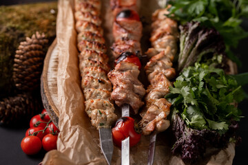 BBQ Healthy barbecued lean cubed pork and chicken kebab on skewers with vegetables, fresh lettuce and tomato salad, close up view on a dark background. Food for a picnic.