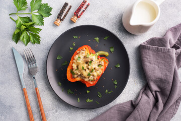Stuffed sweet peppers with rice mushrooms and cheese with herbs. Baked halves of red pepper with filling. Grey concrete background.