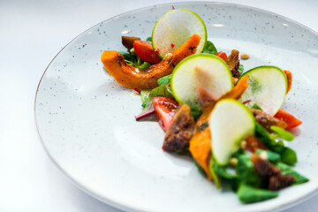 Delicious green fresh salad with backed pumpkin on the white plate, vegetarian food