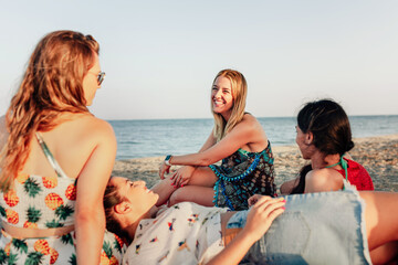 Young women lying on beach, smiling and talking over big scarf