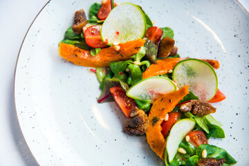 Delicious green fresh salad with backed pumpkin on the white plate, vegetarian food