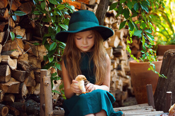 Obraz premium a girl in a green dress and hat near wooden logs with chickens and rolls and milk in the afternoon