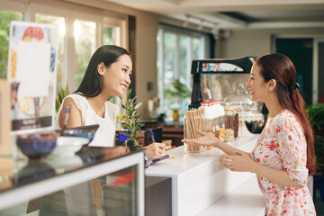 Pretty young Asian woman talkig to barista and ordering coffee and dessert