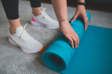 Fototapeta premium Woman rolling yoga mat. Home fitness training concept.
