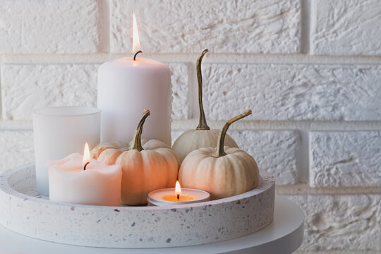 Autumn home decor with white pumpkins and burning candles.