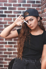 Young caucasian barber woman holding a straight razor and scissors against brick wall