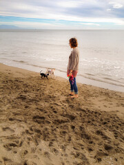 Two dogs playing on the beach with her young female owner