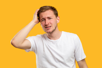 Worried man portrait. Sad memories. Confused guy touching head isolated on orange background.