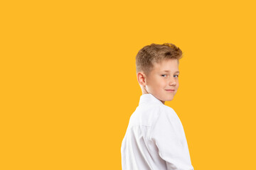 Confident kid portrait. Schoolboy lifestyle. Cheerful boy looking over shoulder isolated on orange...