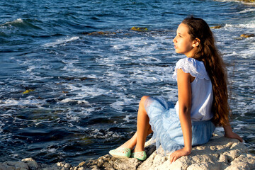 Young beautiful caucasian cute girl outdoor on the seashore on the sand among large beautiful yellow stones