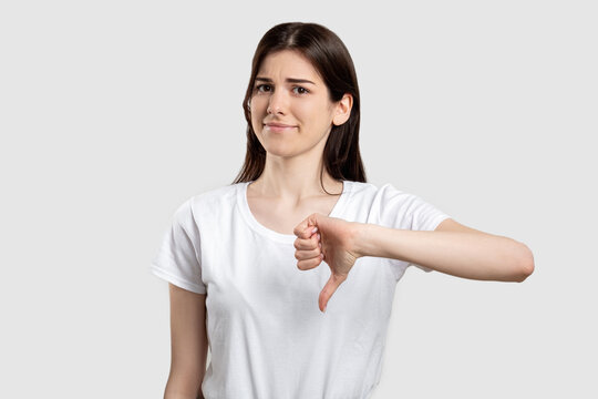 Dislike gesture. Bad idea. Disappointed woman showing thumb down isolated on light background.