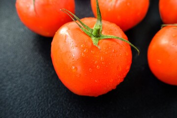 Bright juicy red tomato on a black background with leaves and trunk.