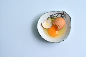 Cracked eggs with egg yolk in ceramic bowl