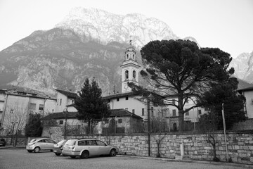 Catholic ancient temple of the 13th century in a small Italian town. Mountains, trees, old town Chiavenna. Italy, Lombardy, August 2017. Black and white photo of church.