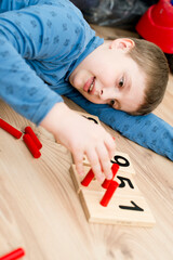 Boy lying on the floor and playing counting game "insert a stick ". Play and learn. Mathematical tasks. Basic addition and subtraction.