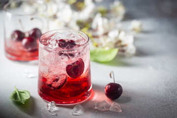 Cold cherry lemonade drink with fresh cherry and ice on gray background