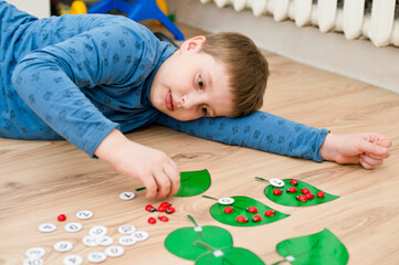 Boy lying on the floor and playing homemade counting game " ladybird on the leaf ". Play and learn. mathematical tasks