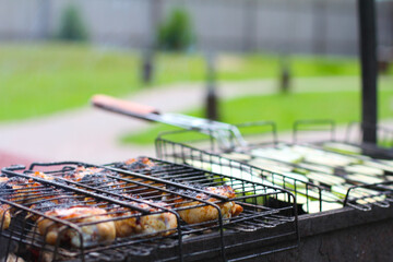 Chiken on a dirty barbecue net. Vegetables on another grill net in blur. Day light. Outdoor