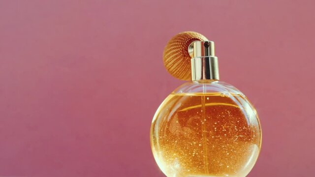 Luxury golden perfume bottle and shining light flares on pink background, glamorous fragrance scent as perfumery product for cosmetic and beauty brand, stock footage