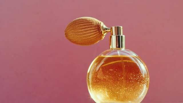Luxury golden perfume bottle and shining light flares on pink background, glamorous fragrance scent as perfumery product for cosmetic and beauty brand, stock footage