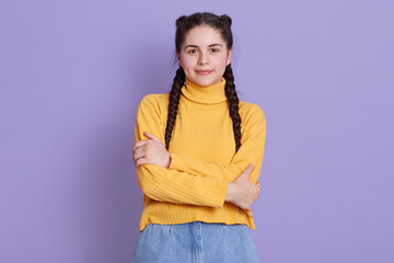 Portrait of brunette female with creative braid hairdo, lady looking directly at camera, wearing yellow sweater, posing isolated over lilac background.