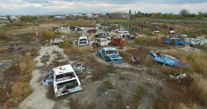 Aerial shot abandoned car dump on the field. Drone's camera slowly fly over many old retro rusty abandoned cars. In background blue sky.