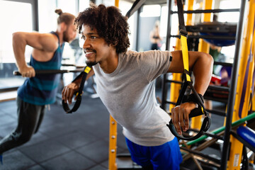 Handsome fit man having fitness TRX training at gym