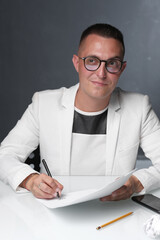 A businessman of 30-35 years old in a white jacket signs important documents.