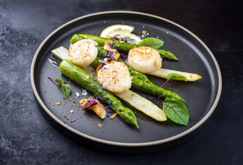 Traditionelle gegrillte Jakobsmuscheln mit grünen und weißen Spargel angeboten als close-up auf enem Modern Design Teller